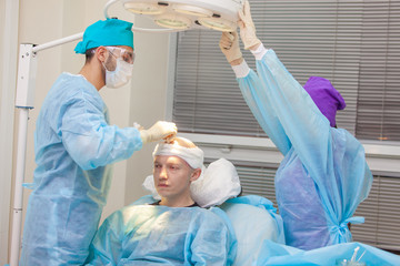 The surgeon directs the lamp light. Baldness treatment. Hair transplant. Surgeons in the operating...