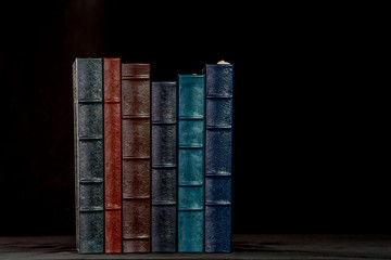 A stack of beautiful leather bound books with a black background.