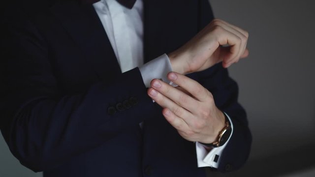 Stylish young man in blue suit adjusts his cufflinks of white shirt. Close-up. Interior. Sunshine. Steady
