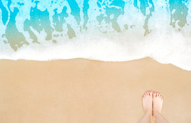 Feet on beach background. Top view on naked feet and legs in sand with wave motion coming to the foot - foaming sea texture. Summer and vacation holiday concept. Selfie barefoot woman standing ocean.