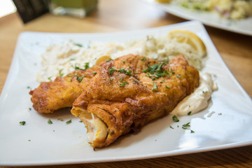 Seelachs Backfisch im Bierteig mit Remoulade, Kartoffelsalat und Krautsalat auf Holztisch 