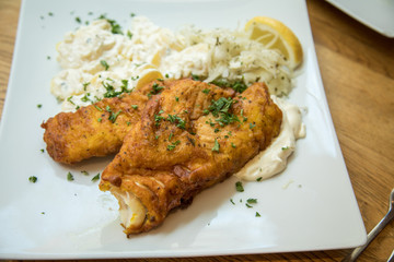 Seelachs Backfisch im Bierteig mit Remoulade, Kartoffelsalat und Krautsalat auf Holztisch 