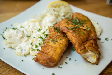 Seelachs Backfisch im Bierteig mit Remoulade, Kartoffelsalat und Krautsalat auf Holztisch 