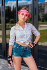 Portrait of an emotional girl in a pink cap visor and protective gloves for rollerblades and skateboarding.