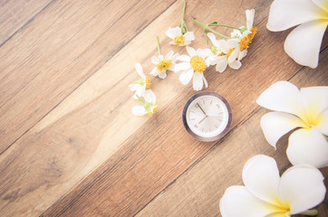 Small table clock with Frangipani flower on wooden table top view.Wooden background with table clock and flowers.
