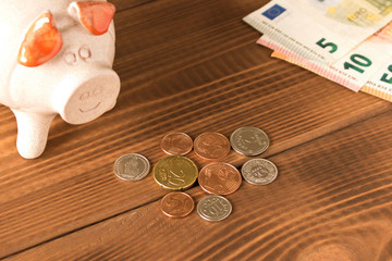 Piggy Bank and a few coins and Euro bills on the wooden table. Close up. The concept of saving money. Selective focus.