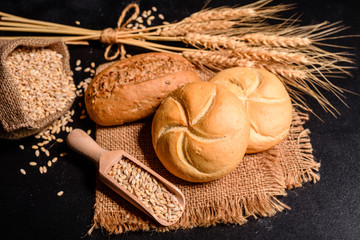 Fresh fragrant bread with grains and cones of wheat against a dark background. Assortment of baked bread on wooden table background. Fresh fragrant bread on the table. Food concept. 