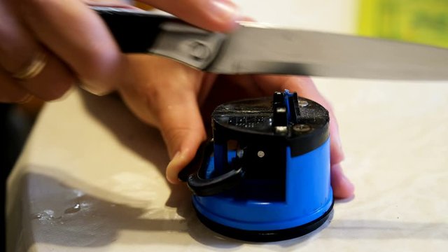 Woman sharpens a kitchen knife. Knife and knife sharpener in the hands of women. Manual sharpening of a knife.