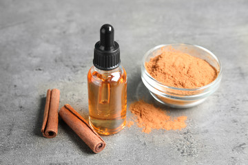 Bottle of essential oil, cinnamon sticks and powder on grey table