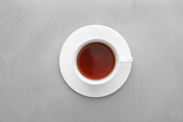Cup of tea and saucer on grey background, top view