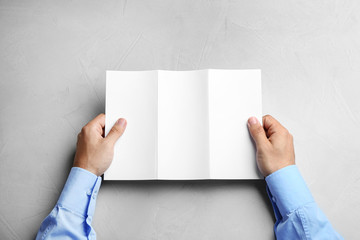 Young man holding blank brochure at grey table, top view. Mock up for design