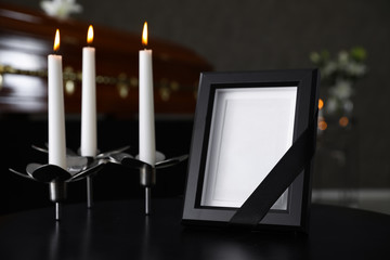 Black photo frame with burning candles on table in funeral home - obrazy, fototapety, plakaty