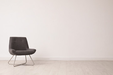 Stylish comfortable chair near white wall, space for text. Interior design