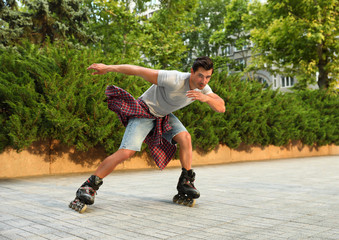 Handsome young man roller skating outdoors. Recreational activity