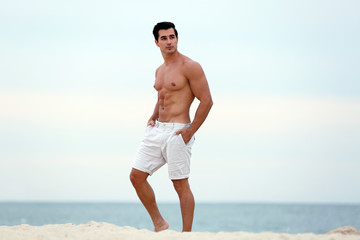 Handsome young man posing on beach near sea