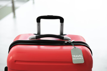 Stylish suitcase with travel insurance label on blurred background, closeup. Space for text
