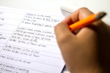 Close-up of boy hand with pencil writing English words by hand on traditional white notepad paper....