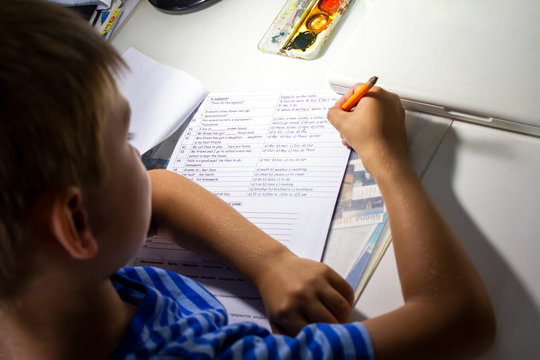 Close-up of boy hand with pencil writing english words by hand on traditional white notepad paper. The boy writes his first letter in English. Child writing - Powered by Adobe