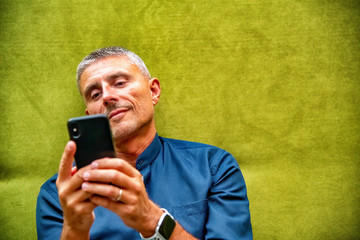 Smiling man texting on smartphone while seated on a green sofa