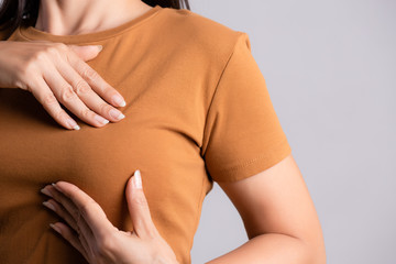 Woman hand checking lumps on her breast for signs of breast cancer on gray background. Healthcare...