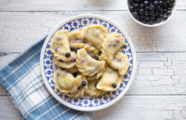 blueberry dumplings, pierogi, vareniki in a clay bowl on a old kitchen table, view from above, flat lay, copy space left