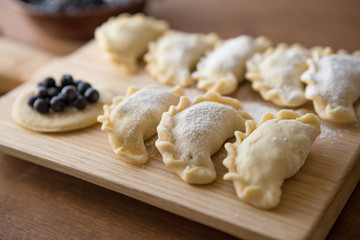 Preparing dumplings filled with blueberry. Elderly female hands making pierogi or pyrohy, varenyky, vareniki. Traditional Ukrainian cuisine, bakery product, sprinkled flour.