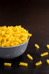 black background with italian raw pasta spiral fusilli in bowl with copy space
