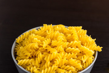 black background with italian raw pasta spiral fusilli in bowl with copy space