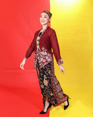 Asian woman traditional maroon kebaya sharong on red yellow paper background walk forward