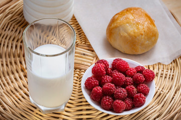 fresh red raspberries, a glass of milk and tasty homemade bun for breakfast on a wooden background