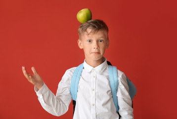Little schoolboy with apple on color background