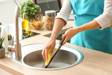 Woman washing wooden board in kitchen sink
