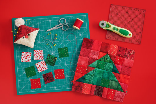 Christmas tree patchwork block, craft mat, bright square pieces of fabric, pincushion like Santa and quilting accessories on red background