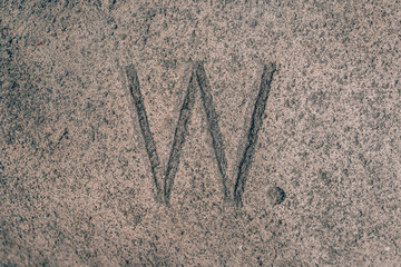 Sign W carved on the stone. Letter of the alphabet on granite. Stone engraving