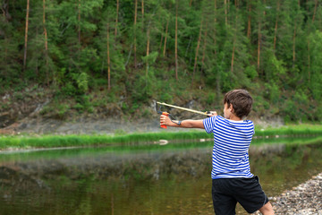 The boy is going to shoot from a slingshot. 9-year-old boy with a slingshot in hands on a...