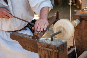 An artisan carves a piece of wood using an ancient lathe driven with pedal.