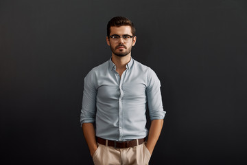 Obraz premium Team lead. Handsome and young bearded man looking at camera and keeping arms in pockets while standing against dark background
