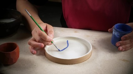 A craftswoman in a workshop paints a freshly prepared plate. Handwork