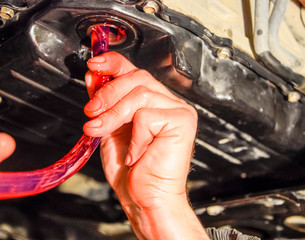 Oil change in automatic transmission. Filling the oil through the hose. Car maintenance station. Red gear oil. The hands of the car mechanic in oil