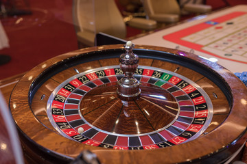 Roulette table in casino, with many games and slots, roulette wheel in the foreground. Golden and luxury light, casino interior. Gambling is the wagering of money or playing games of chance for money