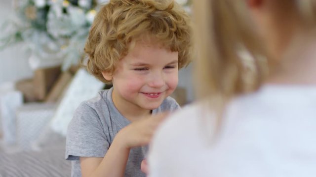 Over the shoulder shot of joyous little boy covering eyes with hands and then receiving Christmas gift from sister and giving hugs to her at home