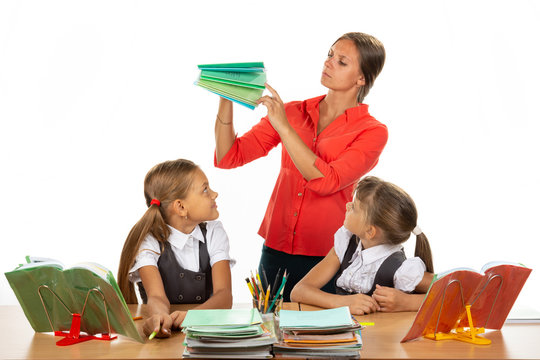 The teacher considers the notebooks of students, two schoolgirls look at her with interest
