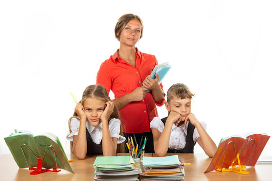 Bored schoolgirls at a desk, in the background a teacher with notebooks