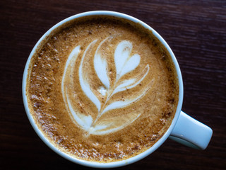 Close up hot cappuccino coffee cup with heart shape latte art on wood table at cafe, tone filter