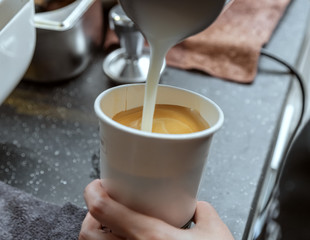 The production of coffee is about to be completed. Pour milk into the espresso. Mix hot milk with concentrate. The barista is making coffee.