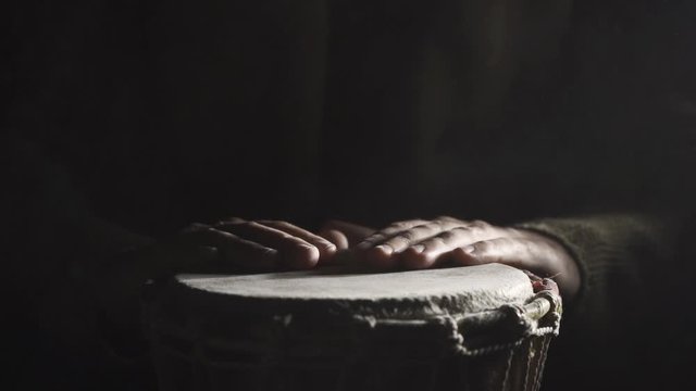 A man playing the djembe drum covered with talcum powder on the dark background, slow motion 2x, front view