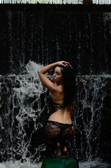 Fototapeta premium Young brunette model posing against a waterfall
