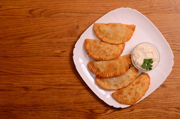 Uzbek eastern Tatar cuisine, cheburek with meat and suluguni cheese in a white plate with vegetables and greens on a wooden table.