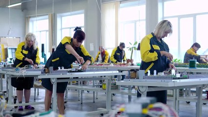 women workers in uniform collect low-voltage and high-voltage equipment in the factory floor. Assembling the filling for transformers. 7 women in uniform working in the factory