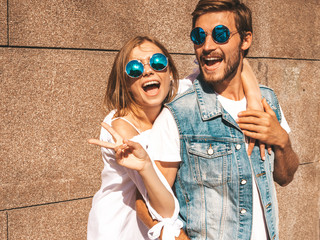 Smiling beautiful girl and her handsome boyfriend. Woman in casual summer dress.Man in jeans clothes.Happy cheerful family.Female having fun on the street near wall.Hugging couple in sunglasses